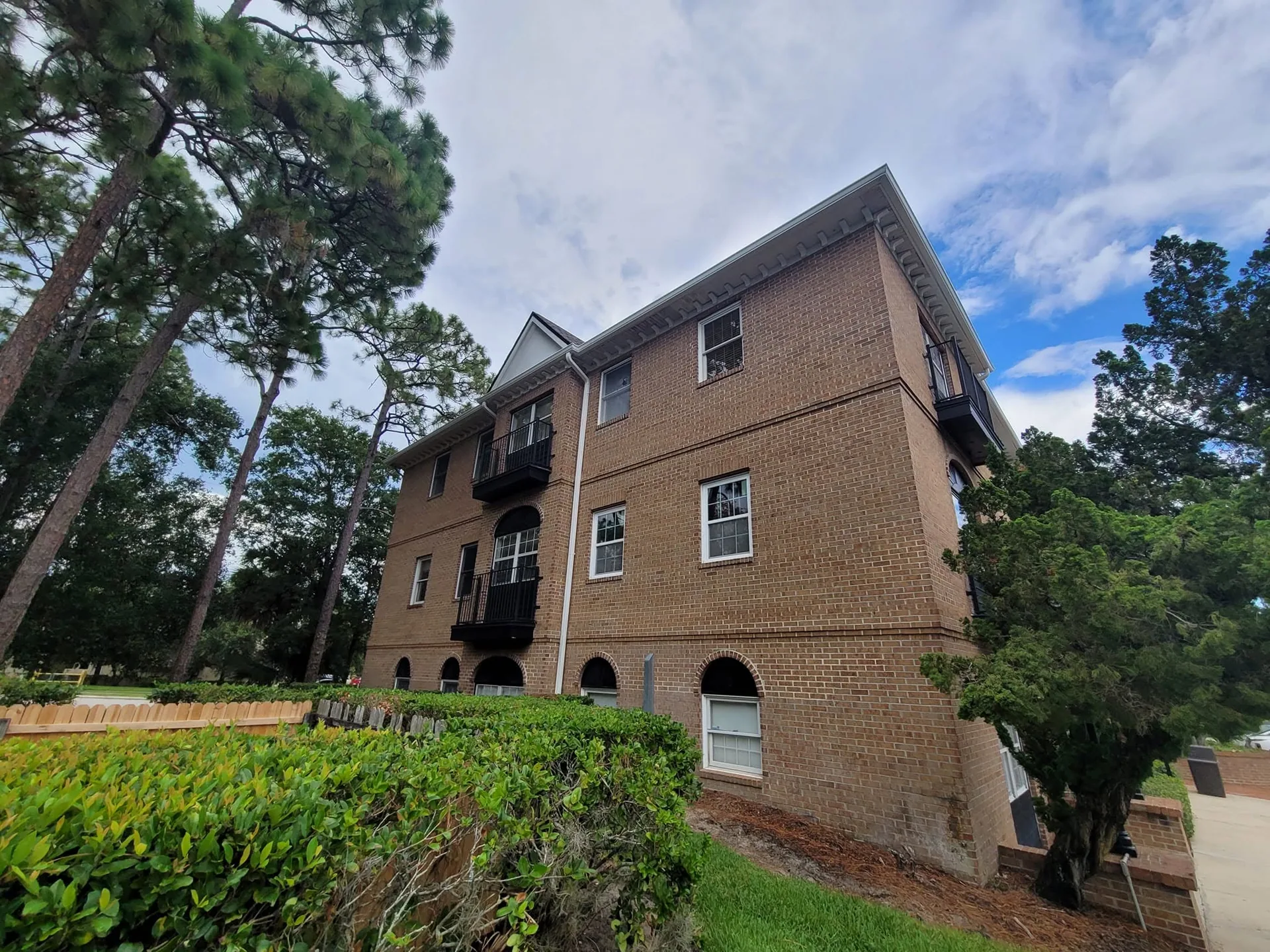 Three story brick building side elevation white downspout juliet balconies hedge